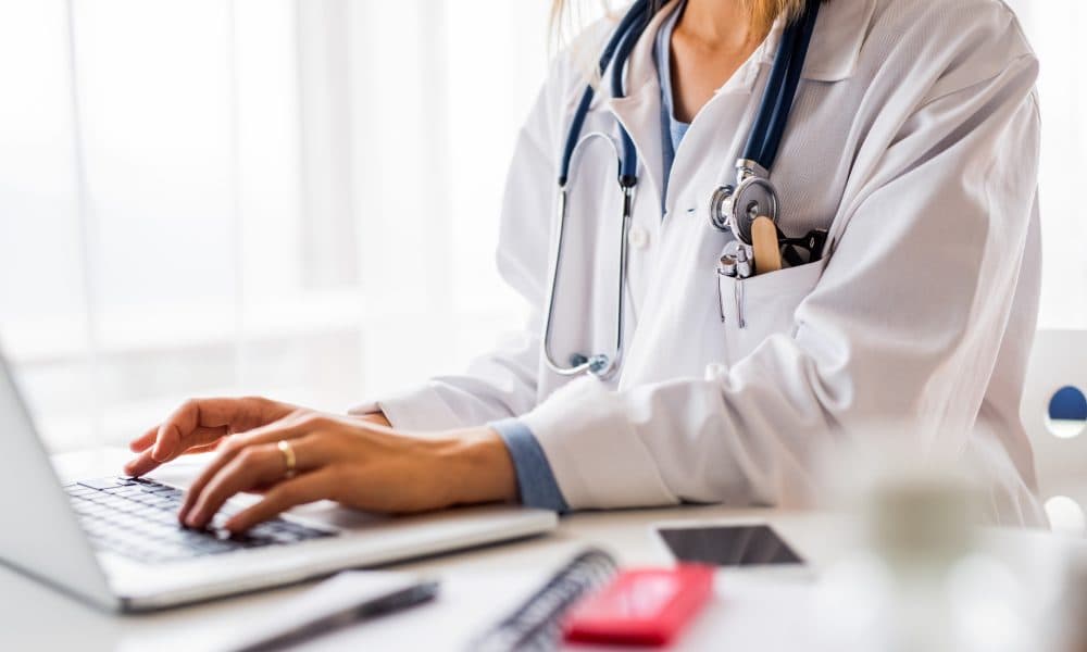 Female doctor with laptop working at the office desk. Oracle buys medical records company Cerner for $28.3bn
