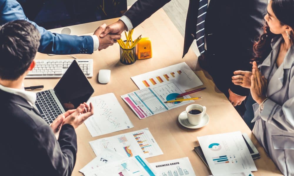 Group business people handshake at meeting table in office together with confident shot from top view . Young businessman and businesswoman workers express agreement of investment deal. Answer Digital acquires healthcare IT organisation Interneuron