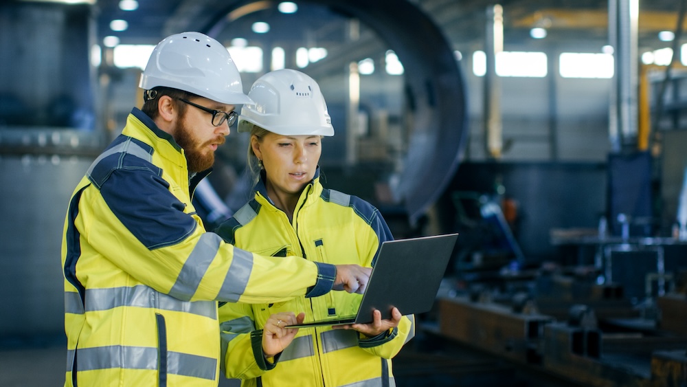 Male and Female Industrial Engineers in Hard Hats Discuss New Project while Using Laptop. They Make Showing Gestures.They Work in a Heavy Industry Manufacturing Factory. Top Safety Tools That Actually Work